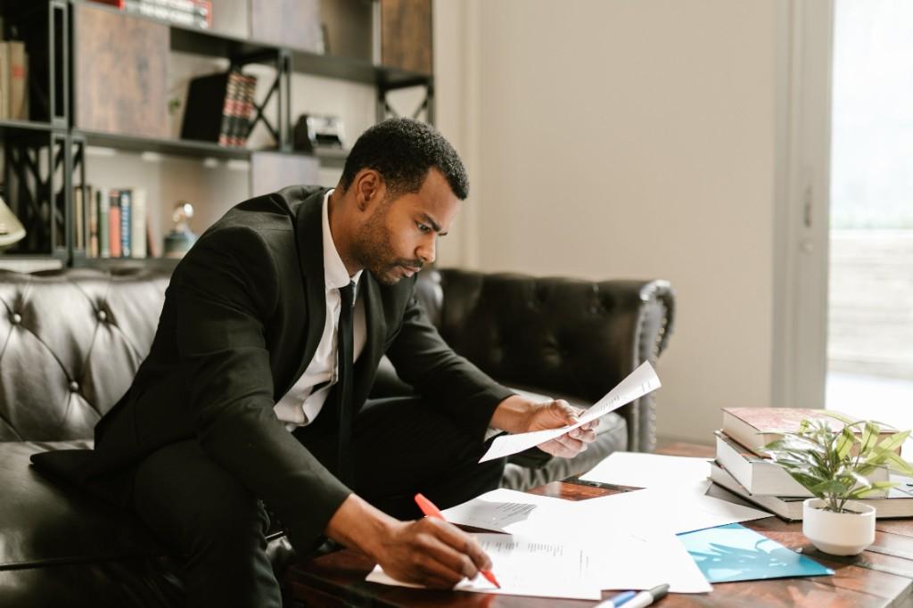 A professional reviewing and marking documents at a desk with books and research materials